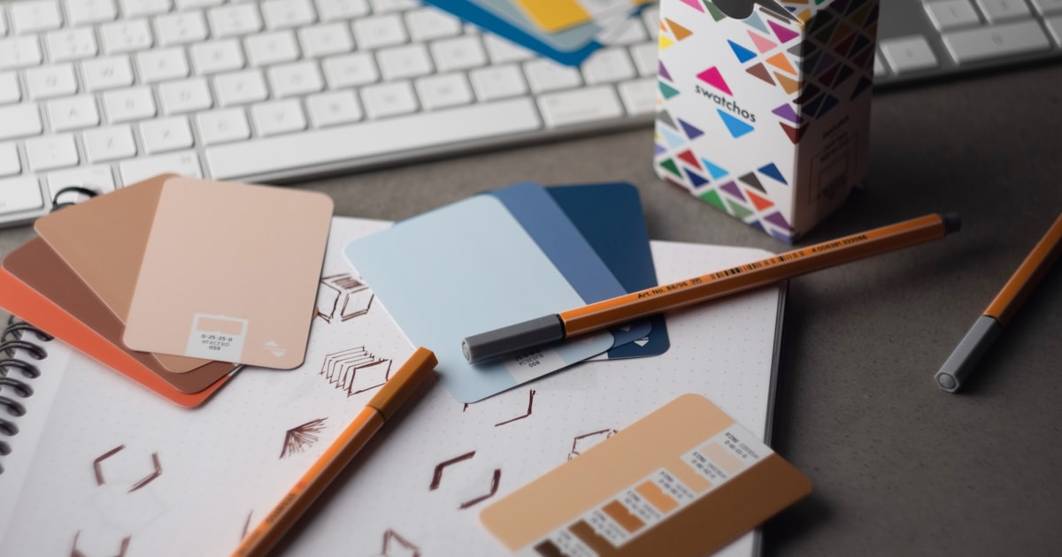 Designer's desk with a keyboard, pencils, and printed colour swatches used for brand palette work